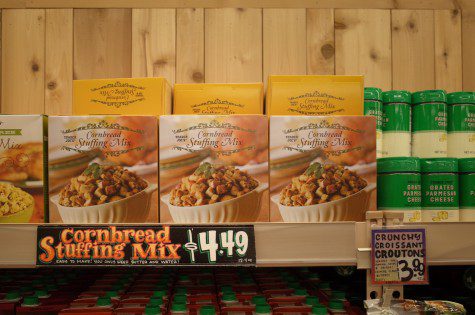 A photo of a shelf labeled “Cornbread Stuffing Mix dollar symbol 4.49,” with seven boxes of cornbread stuffing mix and seven containers of grated parmesan cheese on top.