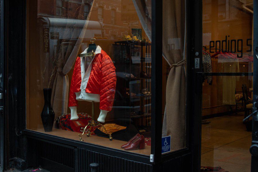 The display window of a store with a red jacket with white collar and sleeves, and a pair of red leather shoes on display.