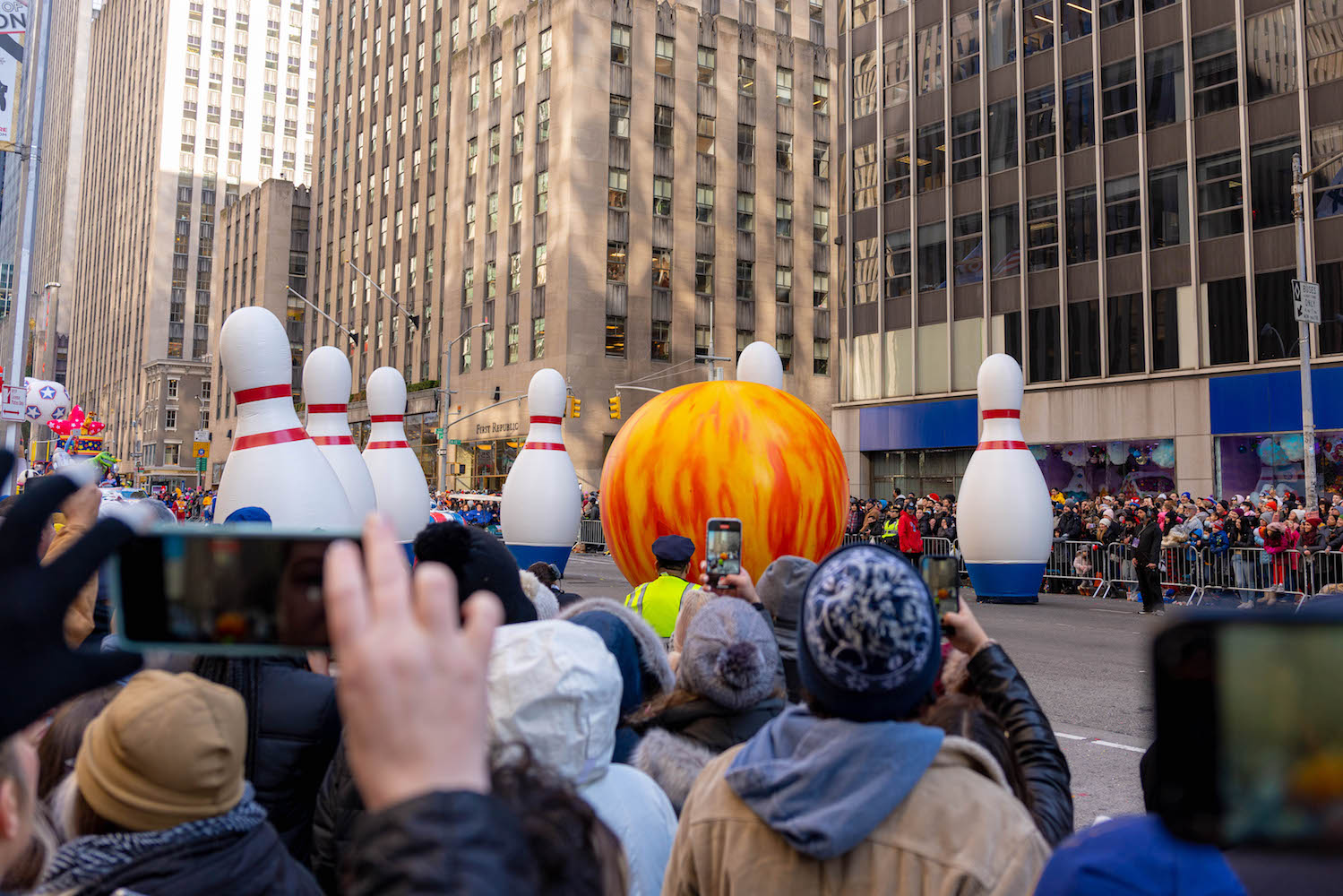 A balloon of a light blue reindeer floating in front of a crowd of bystanders on Sixth Avenue.