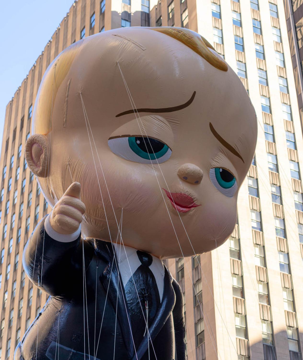 A large balloon in the shape of Boss Baby, a white baby with blond hair dressed in black suit and tie.