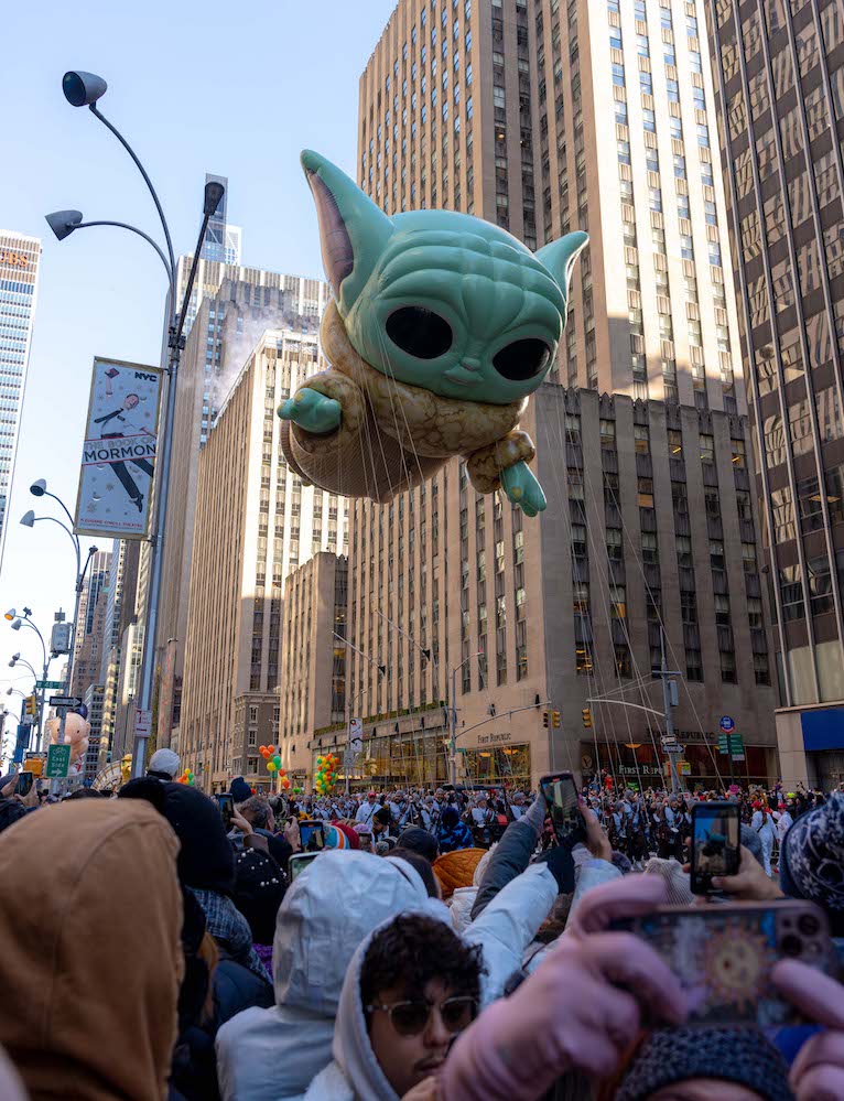 A large balloon of Baby Yoda floating above Sixth Avenue next to the Empire State Building.