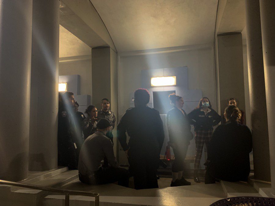 Students and campus safety officers gather in the Third North residence hall courtyard. Two bright lights shine on them from above.