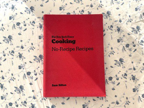 Against a white and blue flowery background is a red-covered book with black titles that read "The New York times Cooking No-Recipe Recipes Sam Sifton."
