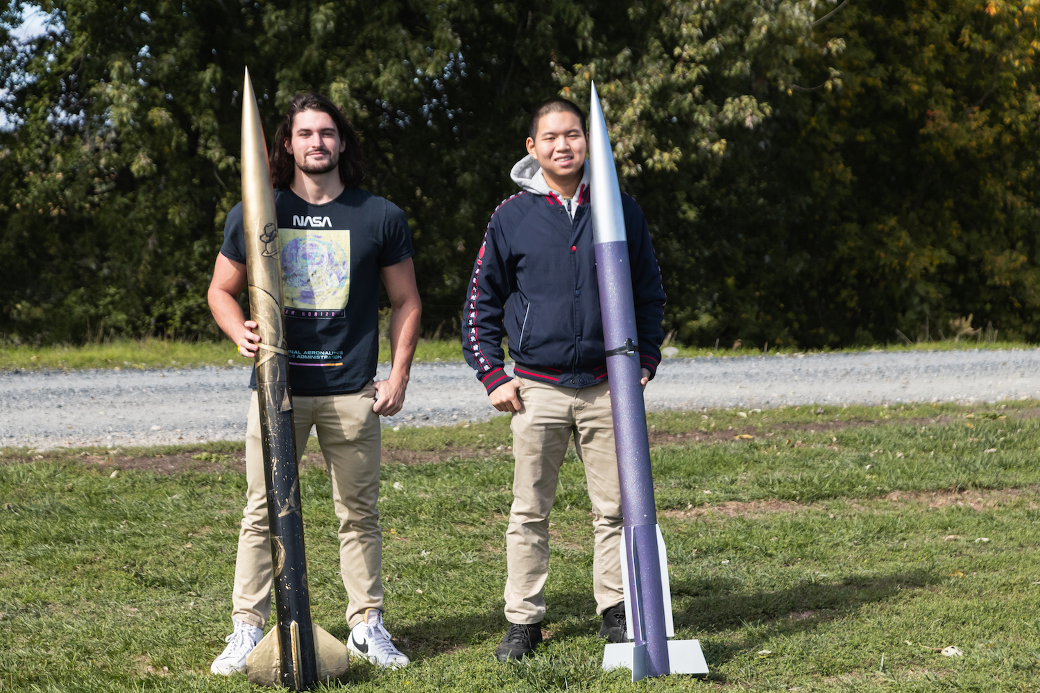 Alex Miller (left) and Alex Xu (right) pose for a photo with their rockets. Miller’s has a gold-and-black design and short angular fins. Xu’s has a purple-and-silver design and straight fins.