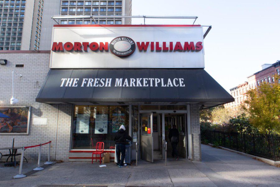 The front entrance of a single-story Morton Williams supermarket. Above the entrance is black awning with the text “THE FRESH MARKETPLACE.”