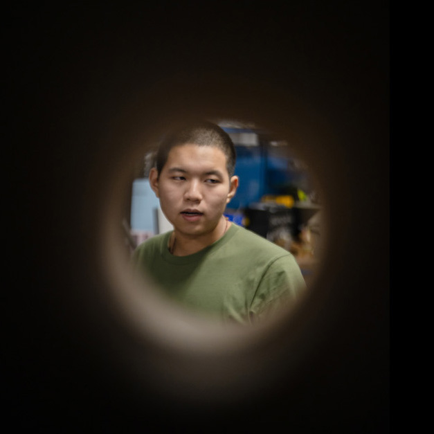 Alex Xu, a young Asian man with short, dark hair wearing a green T-shirt, seen through a tube.