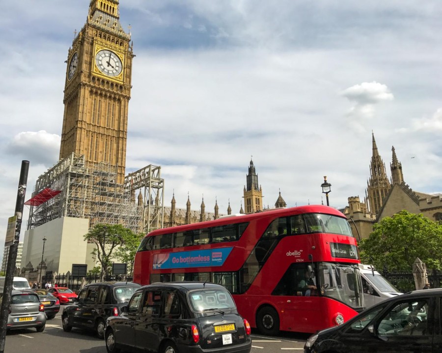 Photograph of a busy London street with cars and a red double-decker bus. Big Ben is seen in the background. It has silver scaffolding around it.