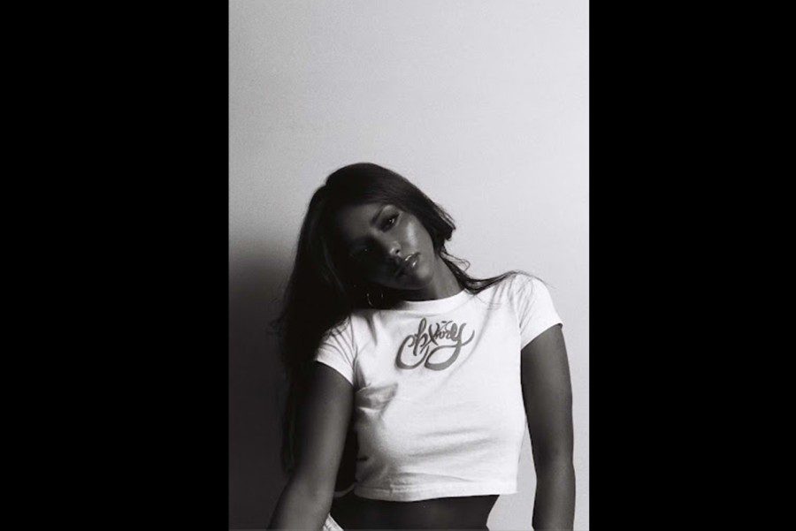 A black-and-white portrait of artist Chxrry 22. A female with dark complexion and black straight long hair poses for picture wearing a white t-shirt that reads “Chxrry” in a cursive font.