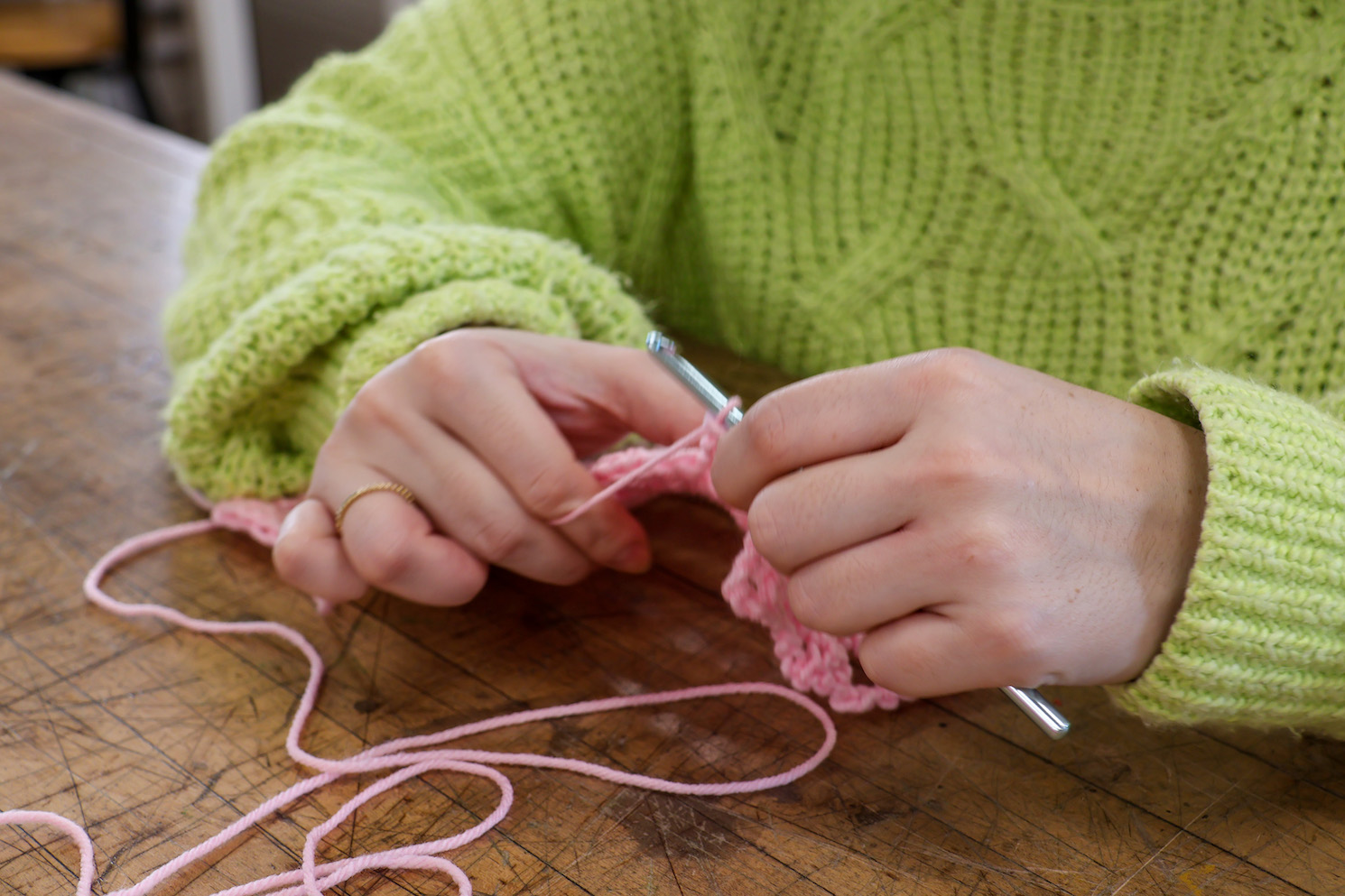 Becca Panes wears a neon green knitted sweater. Becca holds a metallic crochet hook and pink yarns.