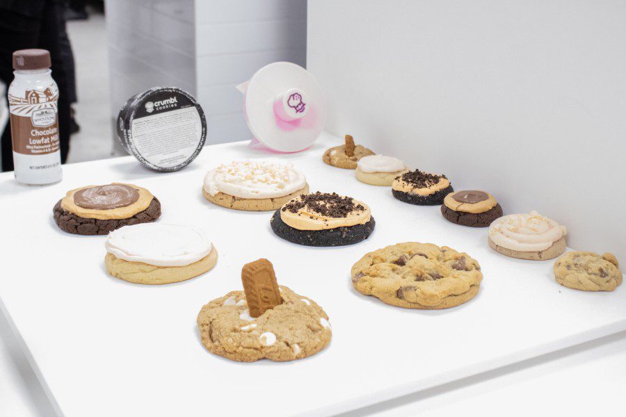 Dozens of cookies laid out on a white table. In the background is a white and brown bottle of low fat milk, a black-and-white can of ice cream, and a pink piece of merchandise. (Jennifer Ren for WSN)