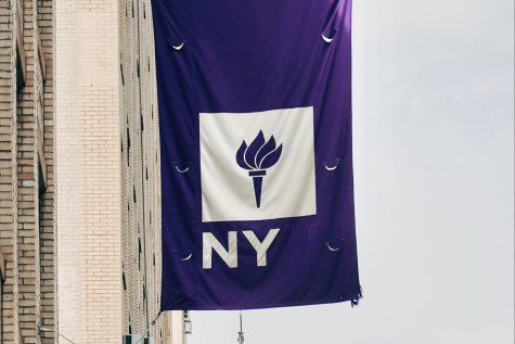 An N.Y.U. flag hangs from the side of a building. The text is white and reads “N.Y.U. The “U” in the banner is faded. The background of the flag is purple.