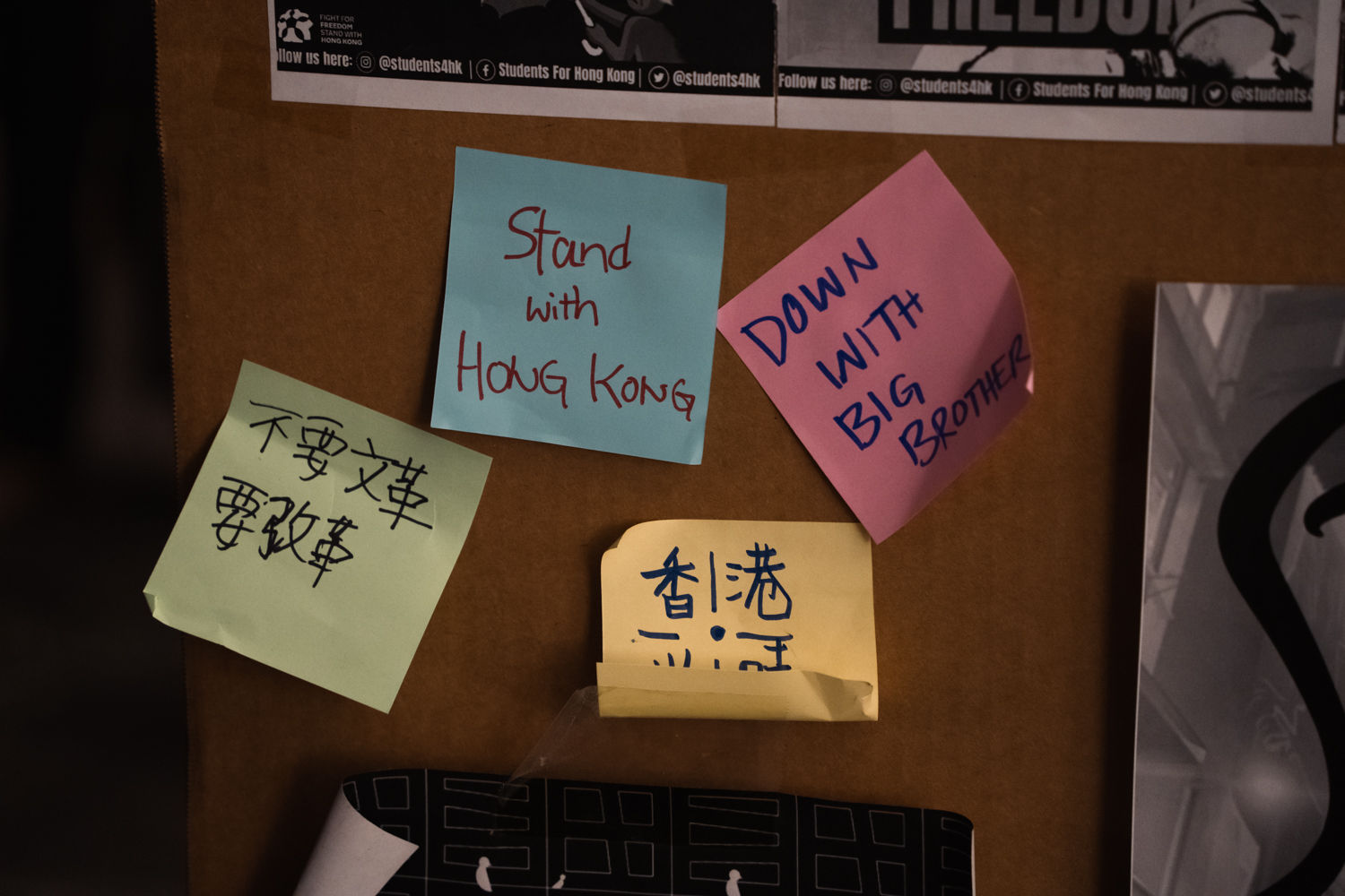 Four sticky notes on cardboard. The green note reads “Say no to cultural revolution, say yes to reform” in simplified Chinese; the blue note reads “Stand with Hong Kong;” the pink note reads “DOWN WITH BIG BROTHER” in all caps; the yellow note reads “Hong Kong” written in Chinese.