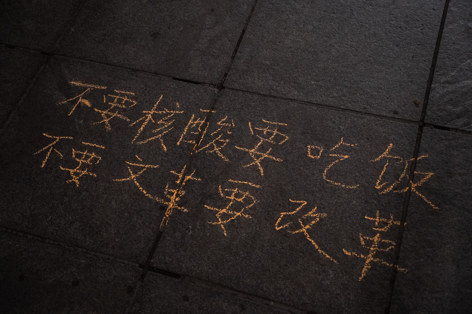 Writings on the ground using orange chalk that reads “Say no to compulsory COVID testing, say yes to livelihood. Say no to culture revolution, say yes to reform” in Chinese.