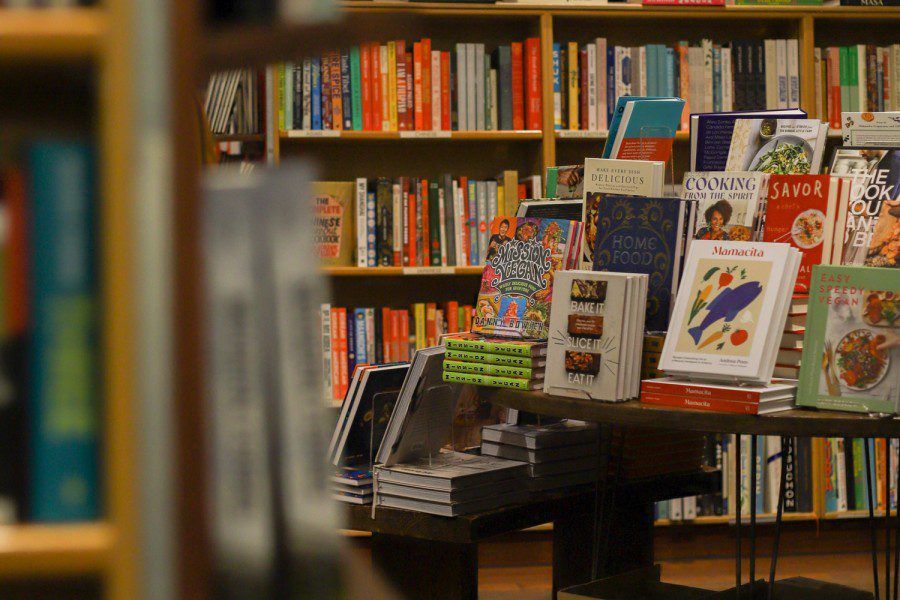 A photo of the interior of a bookstore featuring a bookshelf with titles like “Easy Speedy Vegan,” “Mamacita,” “Bake it Slice it Eat it,” “Mission Vegan,” “Home Food,” “Cooking from the Spirit,” “Make Every Dish Delicious,” among others.