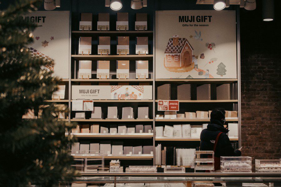 Interior of a store with a large shelf against a brick wall with notebooks of various sizes displayed on it.  In the upper right corner is a large poster with an inscription 