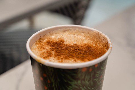 A Goguma latte in a black paper cup with foam and brown powder at the top.
