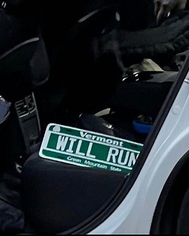 A license plate lying in the back seat of a vehicle. The license plate reads "Vermont. WILL RUN."