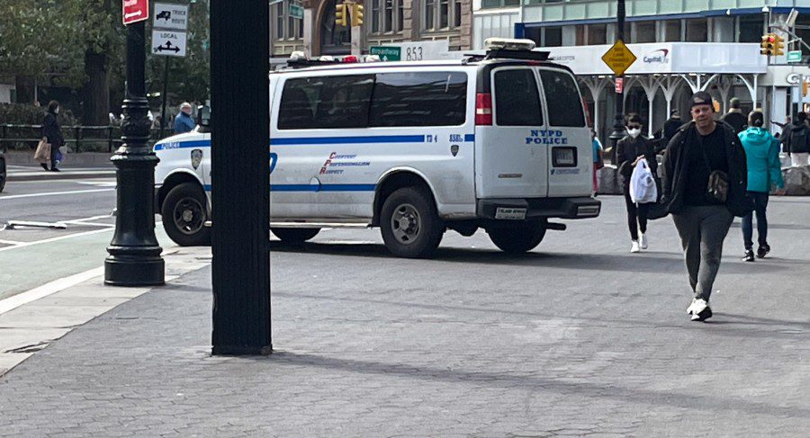 A New York City Police Department van is parked on a public sidewalk. Pedestrians walk past the vehicle near Union Square on East 14th Street.
