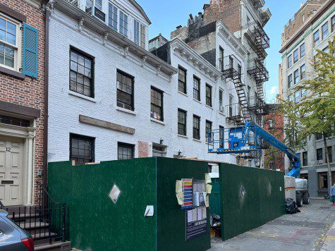 A white apartment building surrounded by green construction fences with a blue crane parked outside the fences.