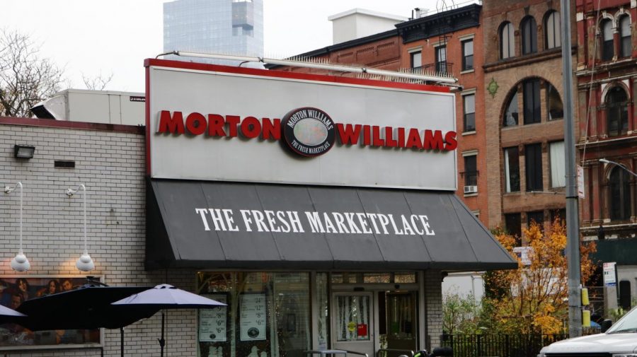 The facade of a gray one-story supermarket is branded with “Morton Williams” in red text. Under the supermarket name, there is text in white letters that reads “The Fresh Marketplace.”