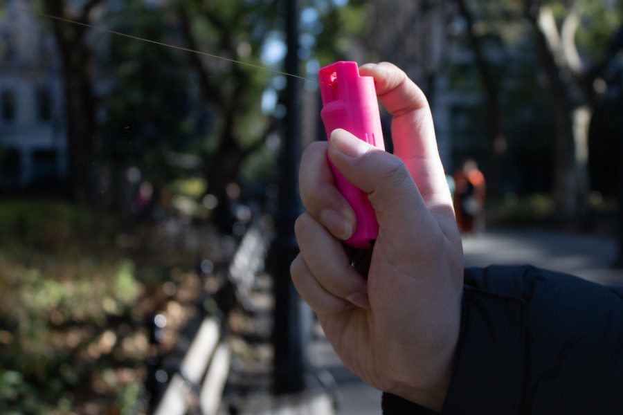 A hand holding a small, pink canister of pepper spray that shoots out liquid.