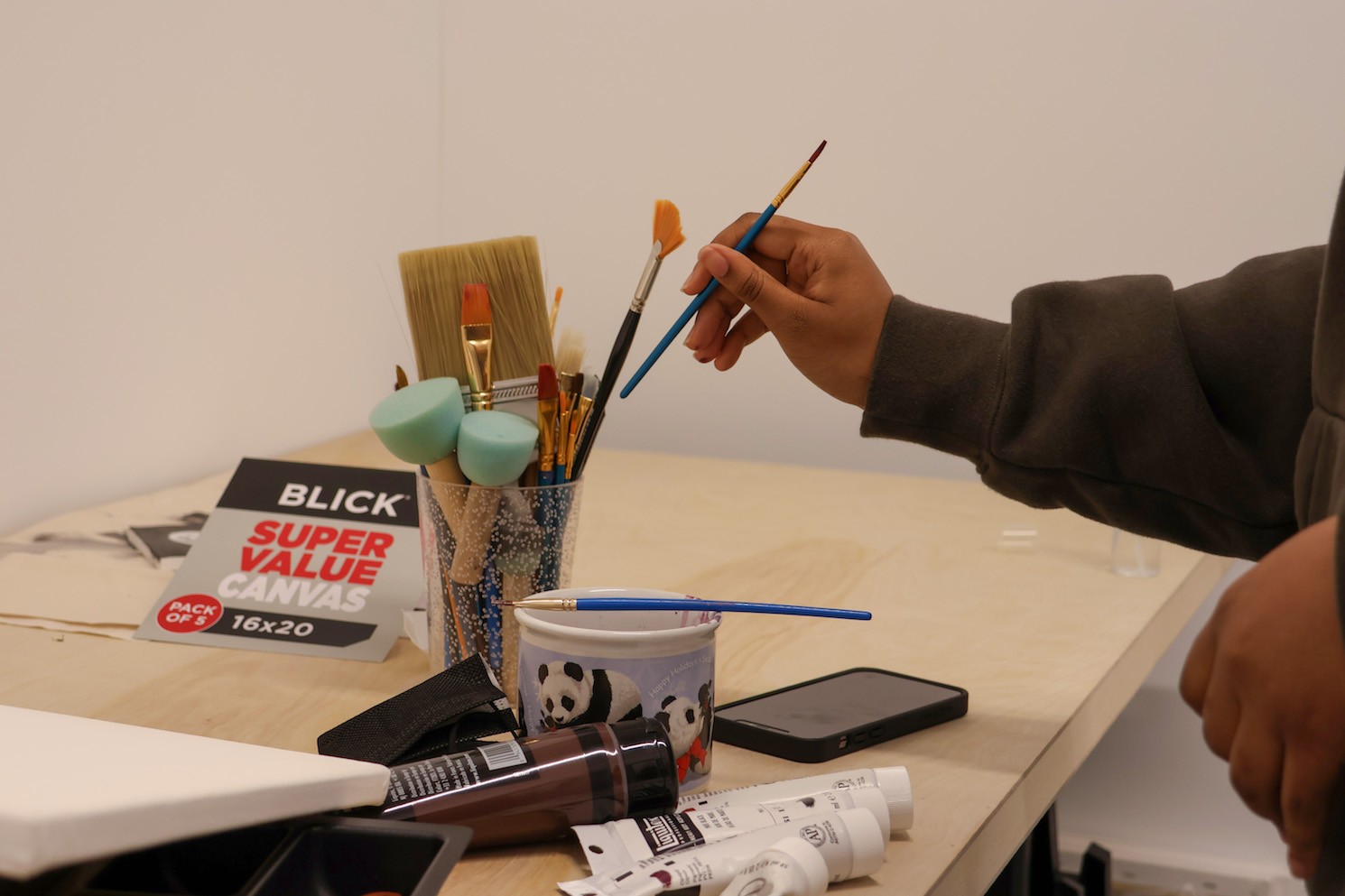Keydi Alvarez pulls out a small-sized brush from a glass filled with an assortment of brushes on the table.