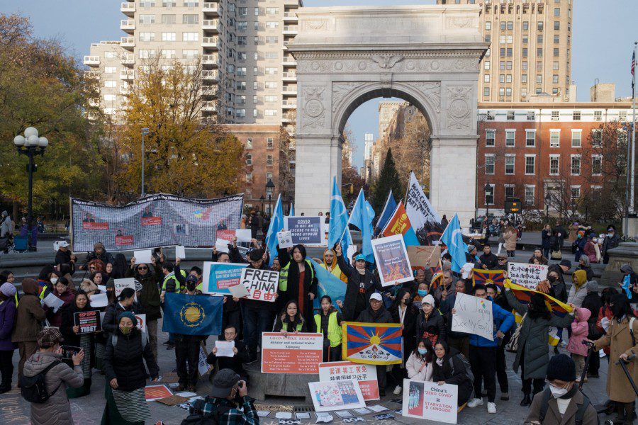 A group of protesters stand inside the fountain at Washington Square Park holding signs that read “Free China” and “COVID is not an excuse to kill more Uyghur lives.” Some are holding Kökbayraq flags and a Tibetan flag.