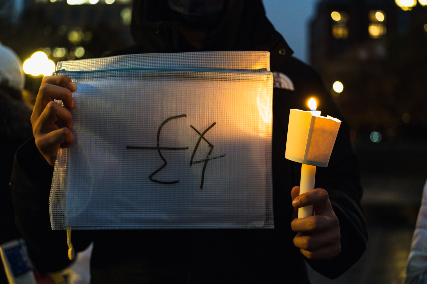 A person wearing black holding a torch in one hand and a plastic bag with the Chinese character for “good” written on it upside down.
