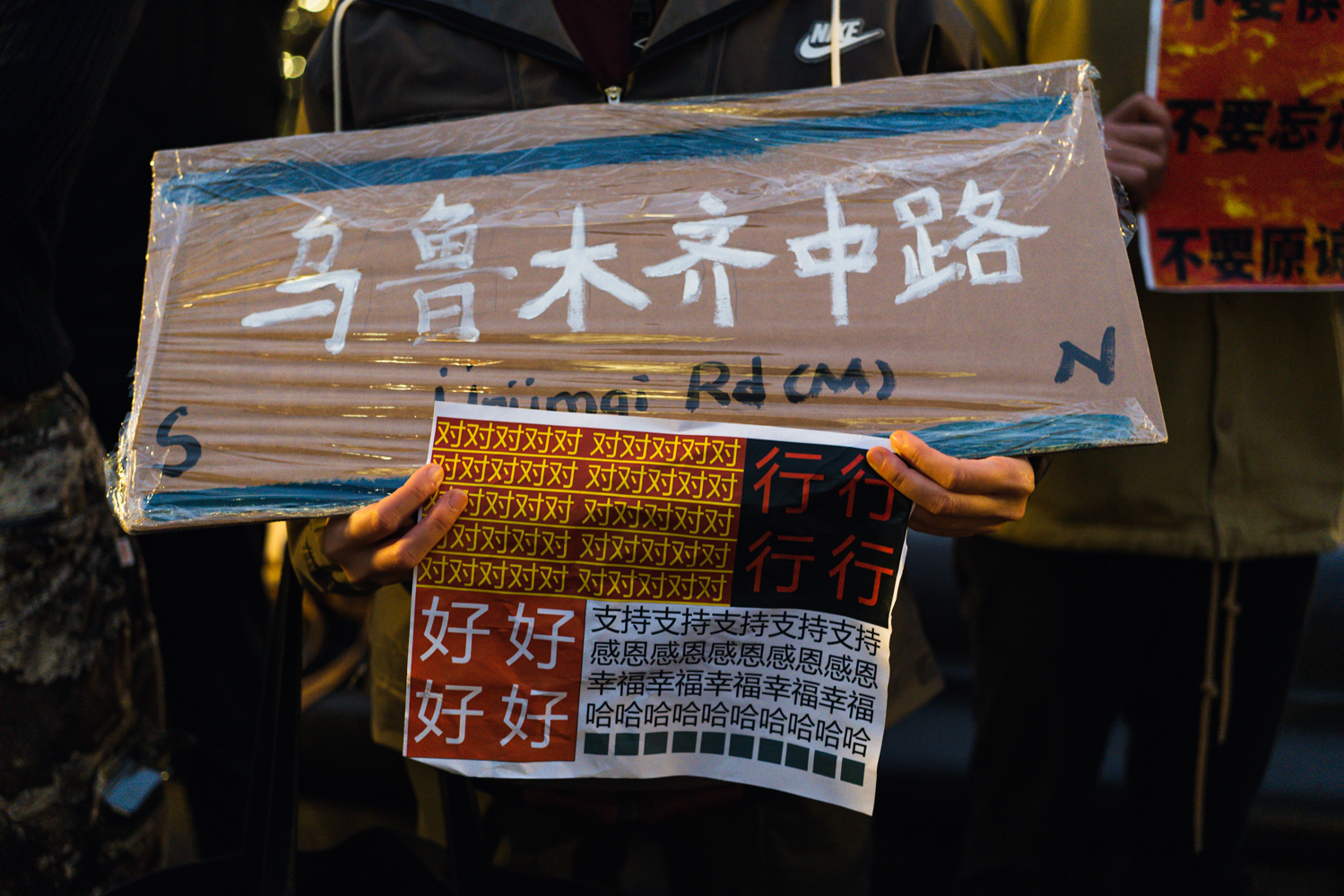 A person holding signs that read “Ürümqi Rd(M)” and “yes, ok, nice, thank you” in Chinese.