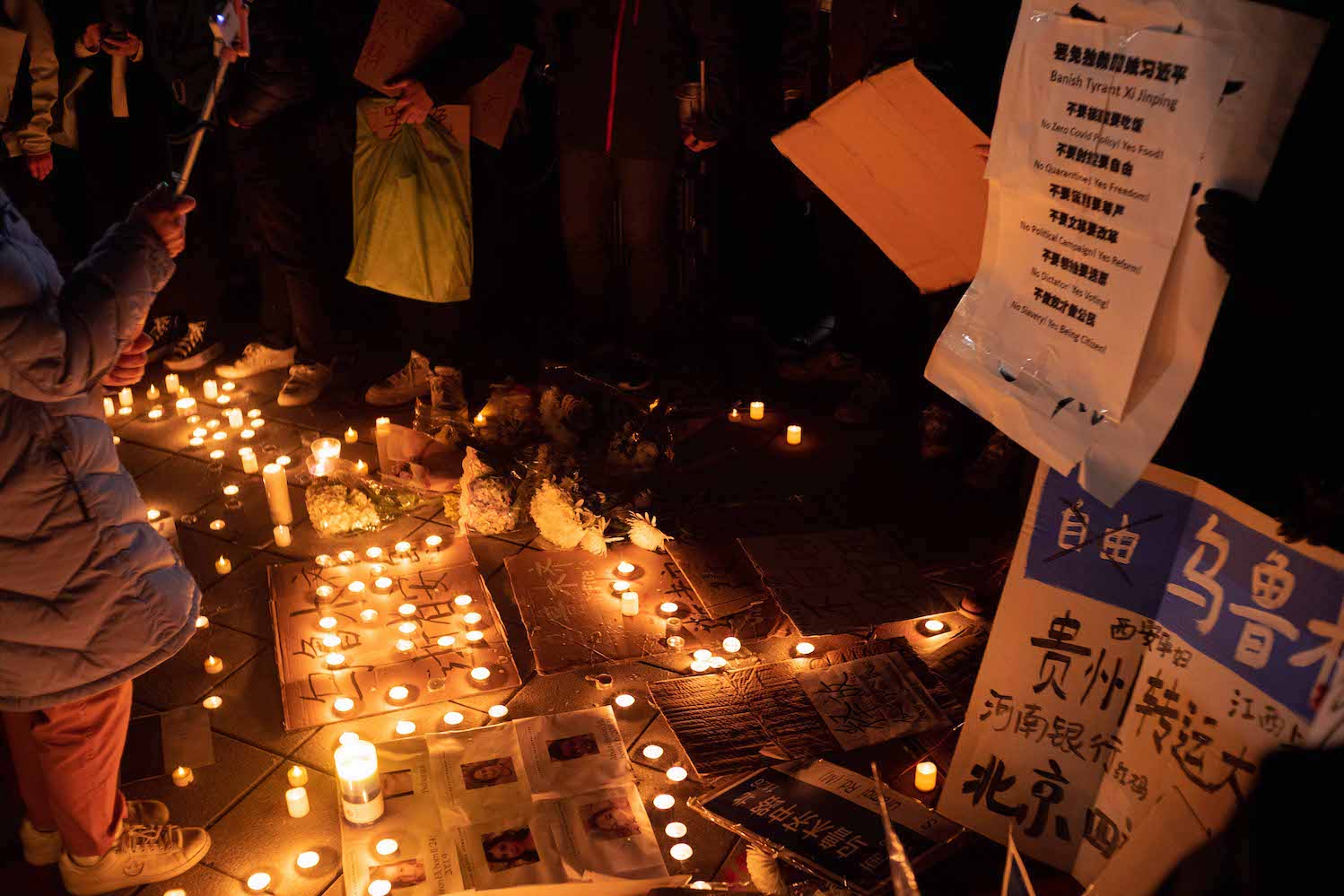 An arrangement of candles laid on the ground with commemorative texts in Mandarin written on posters and papers around the candles.