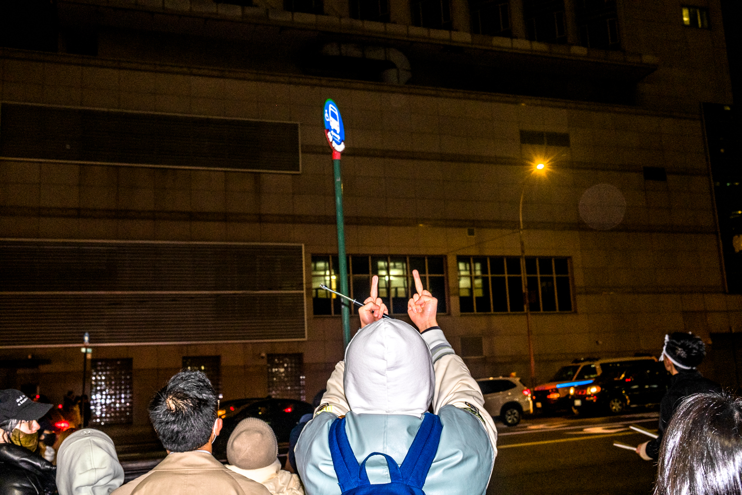 A protester wearing a hoodie shows both of their middle fingers to the Chinese Consulate General.