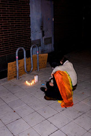 Two protesters sit in front of an arrangement of candles and cardboard written with Mandarin texts.