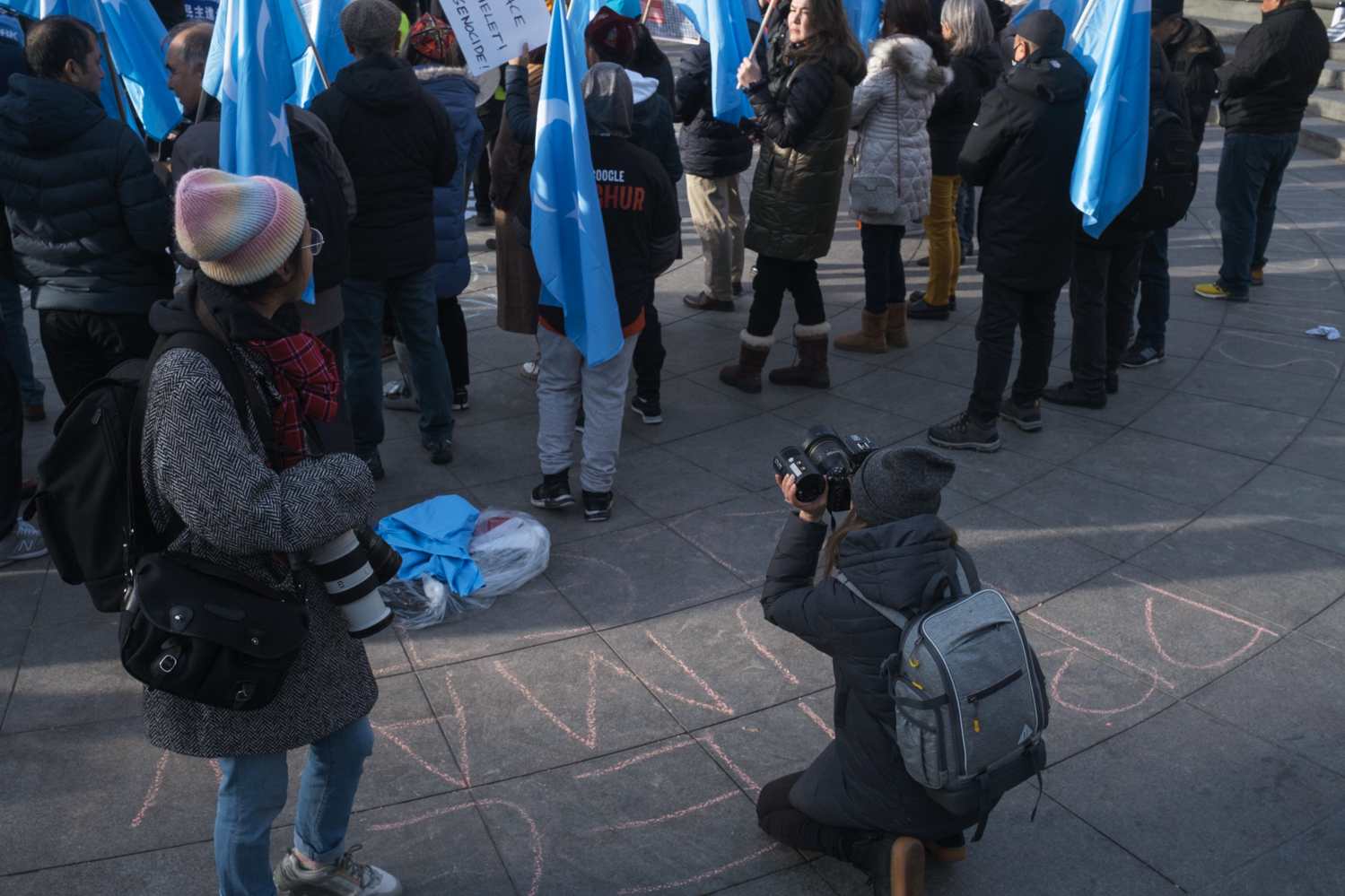 A photographer capturing the backs of Uyghur protesters who wave the light blue flags of East Turkestan.
