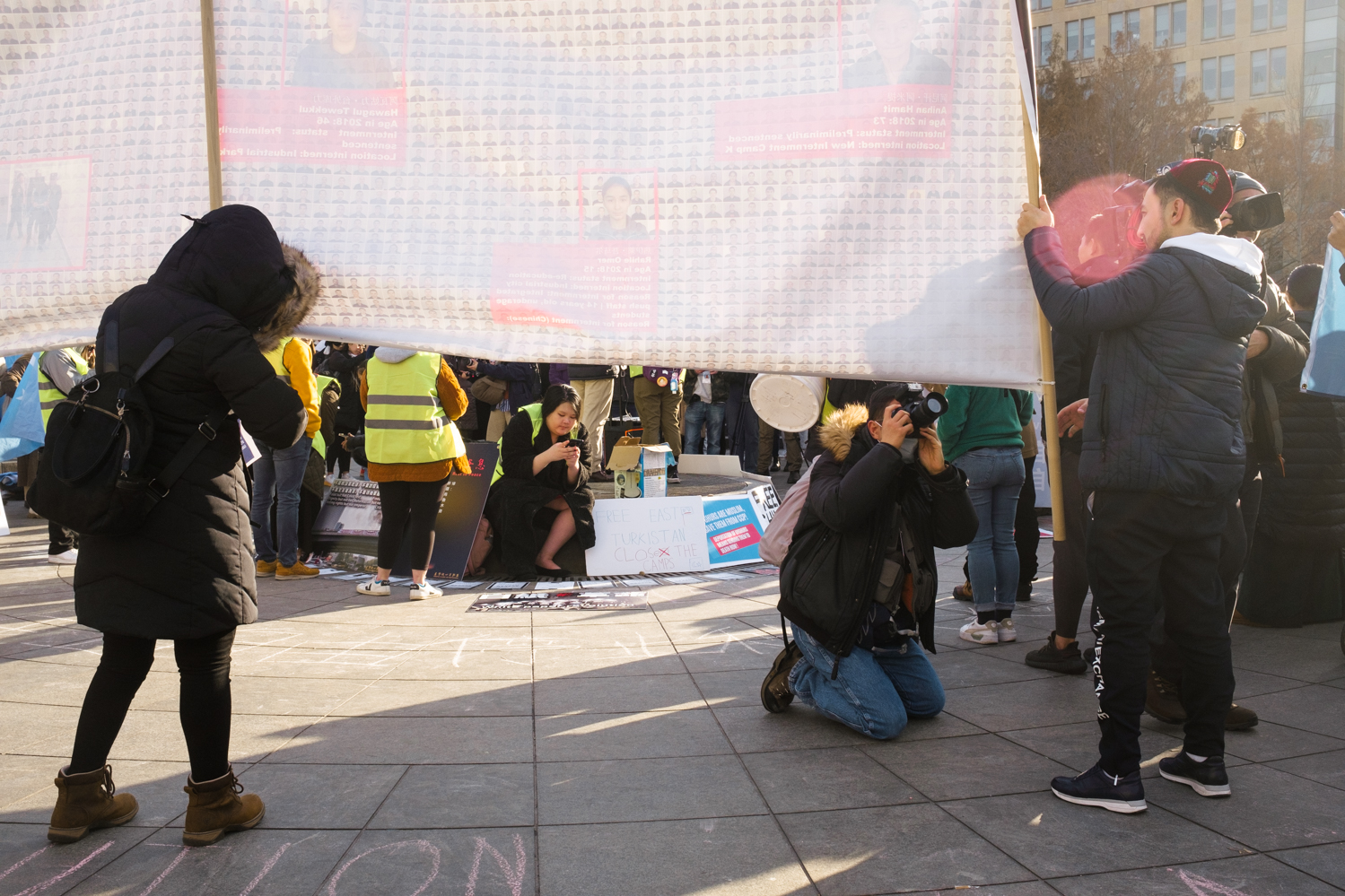 A photographer captures a protester holding up an infographic poster detailing the people detained in internment camps in Xinjiang.