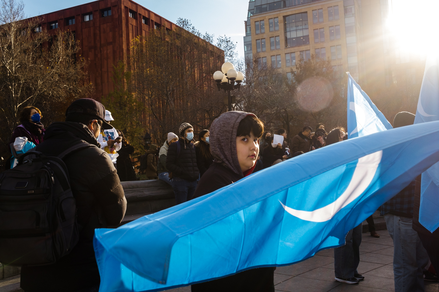A young Uyghur boy waves the East Turkestan flag — blue flags with a white crescent moon and star.