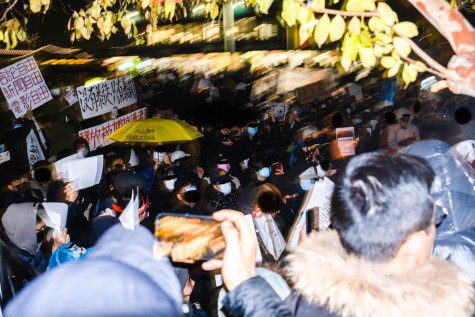 Protesters with most of their heads and faces covered, raise signs in Mandarin.