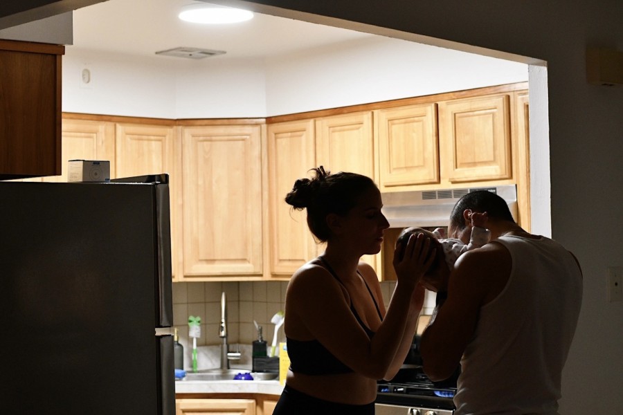 A photo of a couple in a kitchen holding a baby.