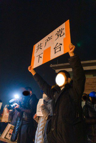 A middle-aged male protester with his face redacted holds an orange sign in Mandarin.