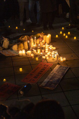 An arrangement of candles, flowers and texts is on the floor in the center of the protest.