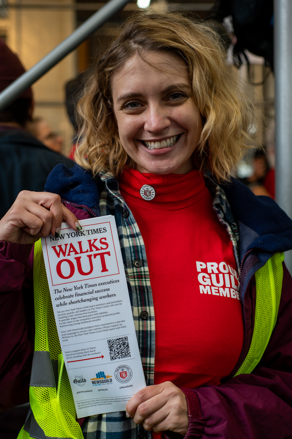 Phoebe Lett, a woman with short blond hair wearing a red shirt, holds a flier that reads “New York Times Walks Out.”
