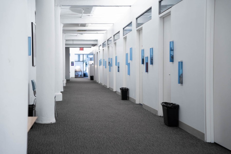 A long, empty stark white office is pictured with little saturation. The only distinct feature is the neon red EXIT sign.