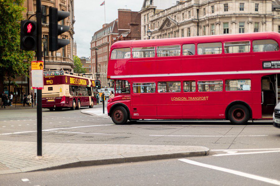 A red double-decker bus, with the text “London Transport” painted on its side, drives around a bend.