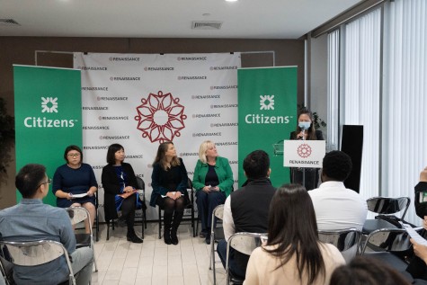 Four people sit in front of two green posters with the word “Citizens'' written over them in white font. In the background is white backdrop with several “Renaissance” logos on top. Next to them is a female speaking behind a transparent podium with a “Renaissance” logo. There is a small group of people sitting in front of them.