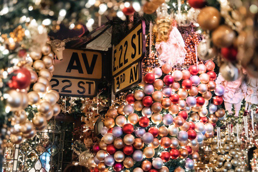 A road sign that reads “the letter E 22 Street” and “Third Avenue” is hung on a wall filled with Christmas decorations.