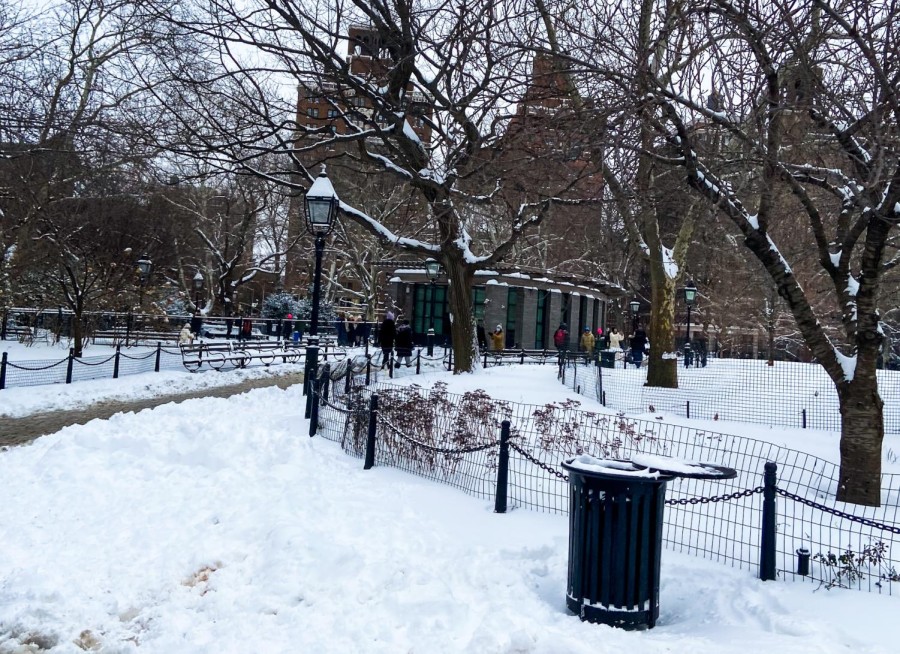 The southwest side of Washington Square Park covered in snow. People walk in the park.