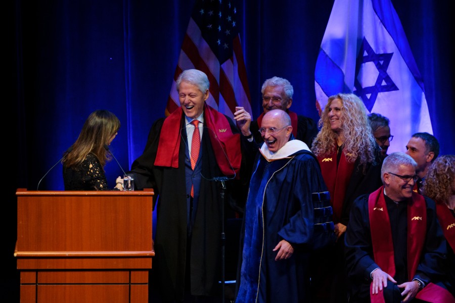 Bill+Clinton+wears+a+navy+blue+suit%2C+a+red+tie+and+a+black+robe+while+laughing+on+stage.+Next+to+Clinton+is+Ron+Robin+also+laughing+in+a+blue+robe.