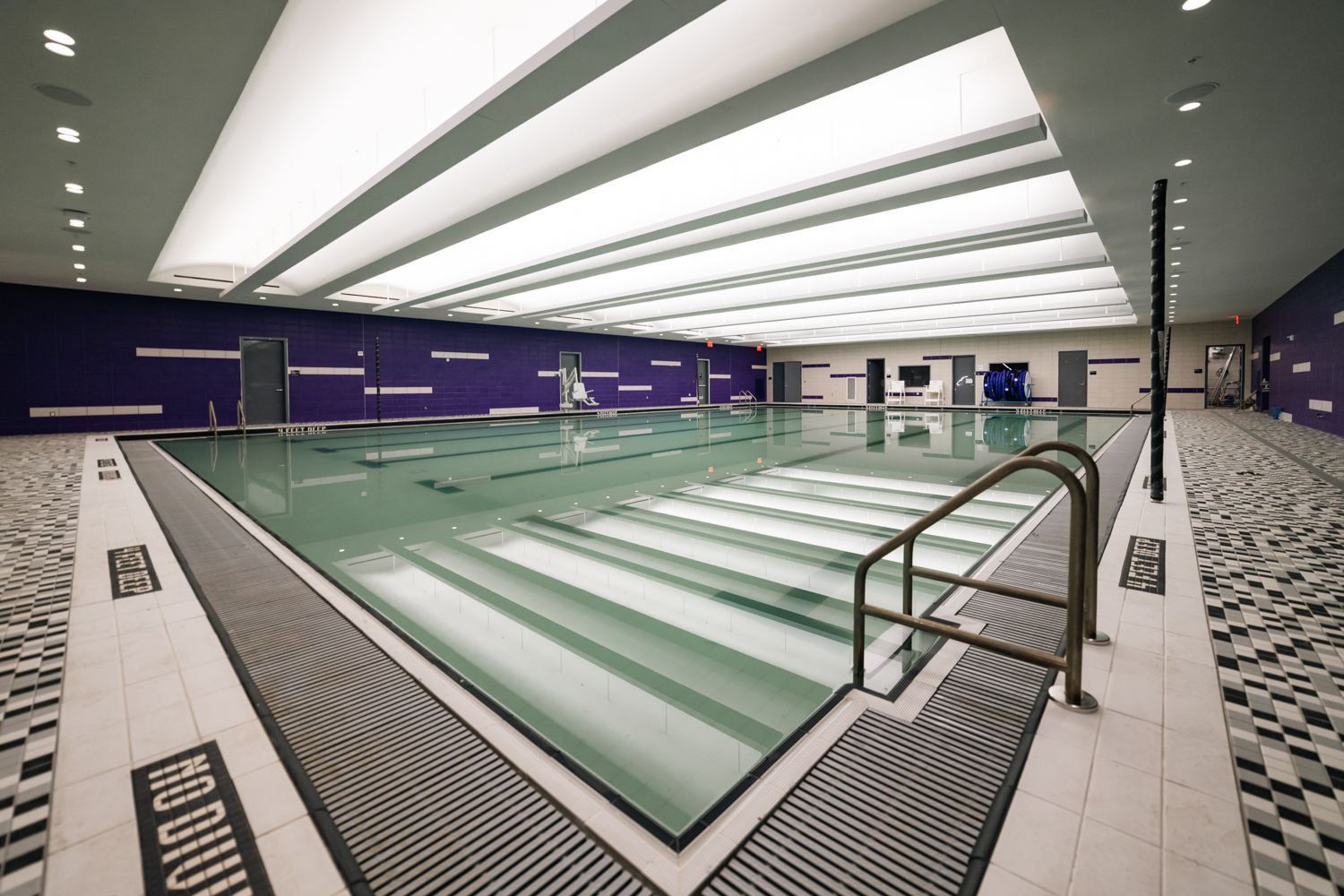 An empty indoor swimming pool with purple walls and a floor with grid patterns surrounding it.