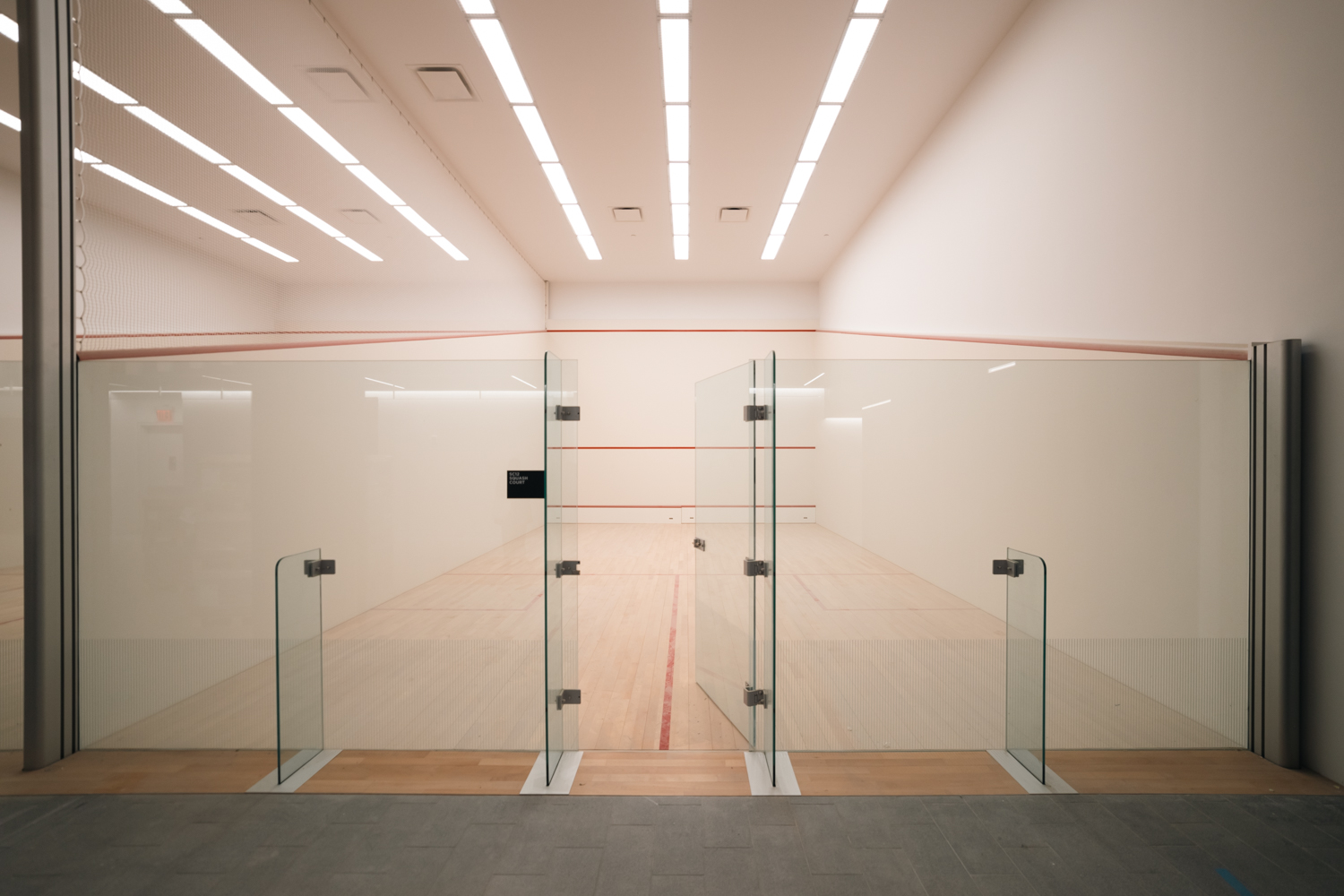 An empty squash court with glass doors and white walls.