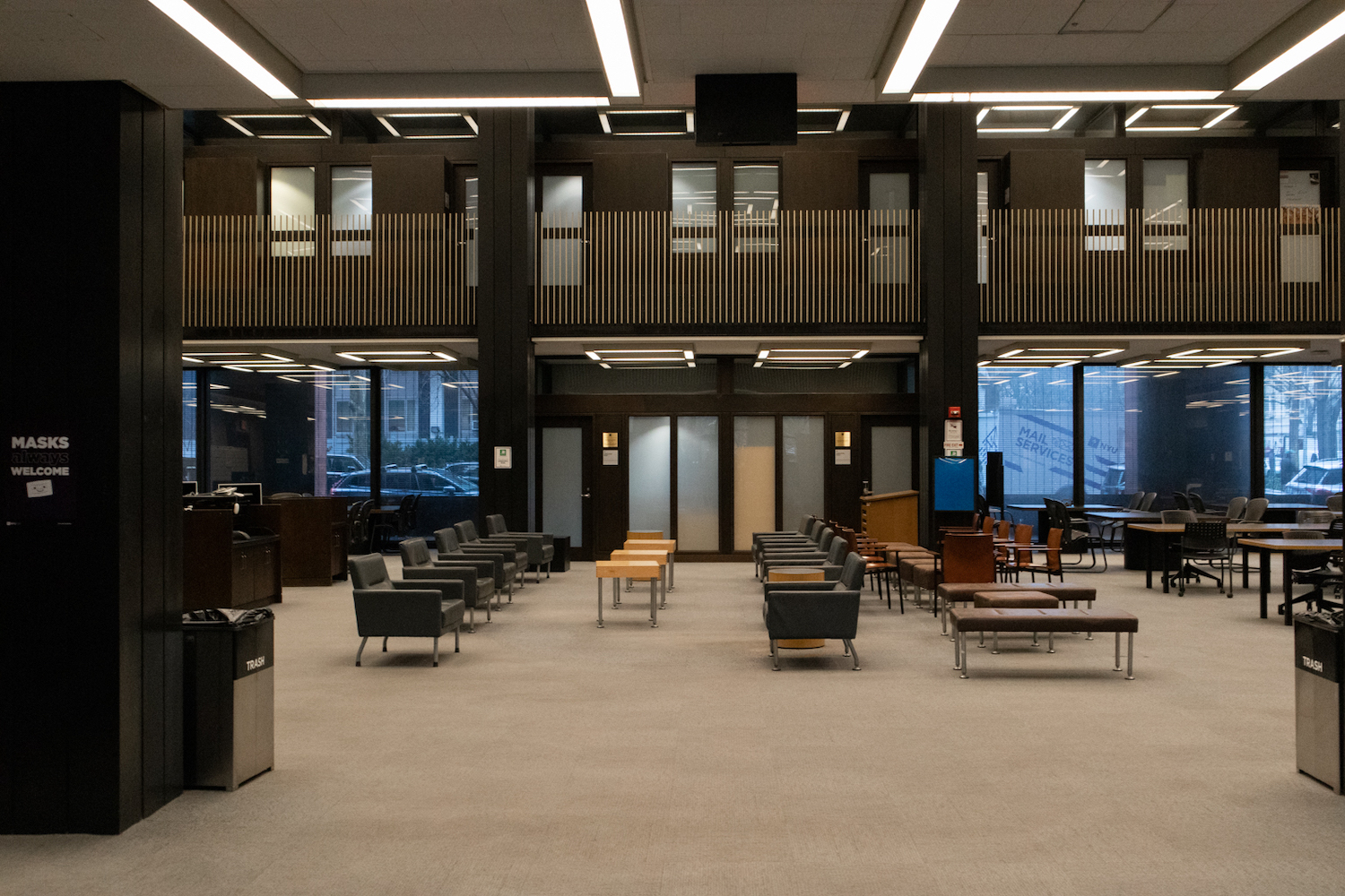 The first floor of Bobst Library, lined with armchairs, benches, tables and windows in the back.