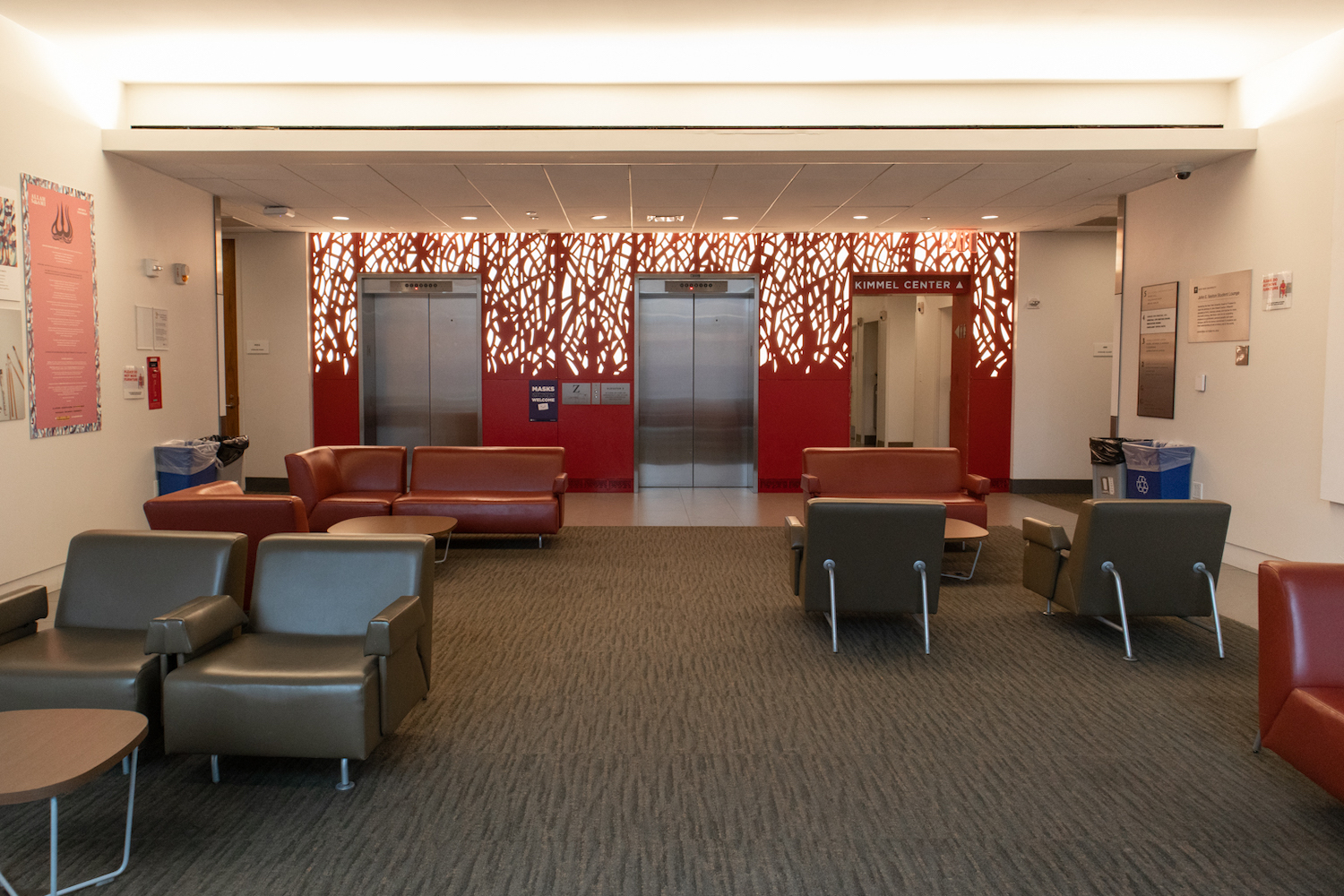 A photo of vacant leather couches in an empty lounge at the NYU Global Center for Academic and Spiritual Life with two elevators against bright red walls.